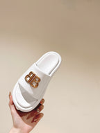 White Balenciaga slide sandal held in hand with gold “BB” logo on strap