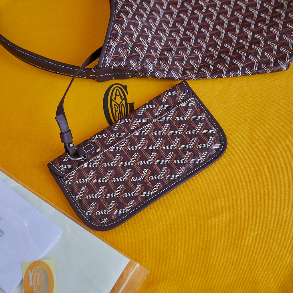 Burgundy patterned Goyard mini pouch wallet with shoulder strap and gold emblem.