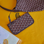 Burgundy patterned Goyard mini pouch wallet with shoulder strap and gold emblem.