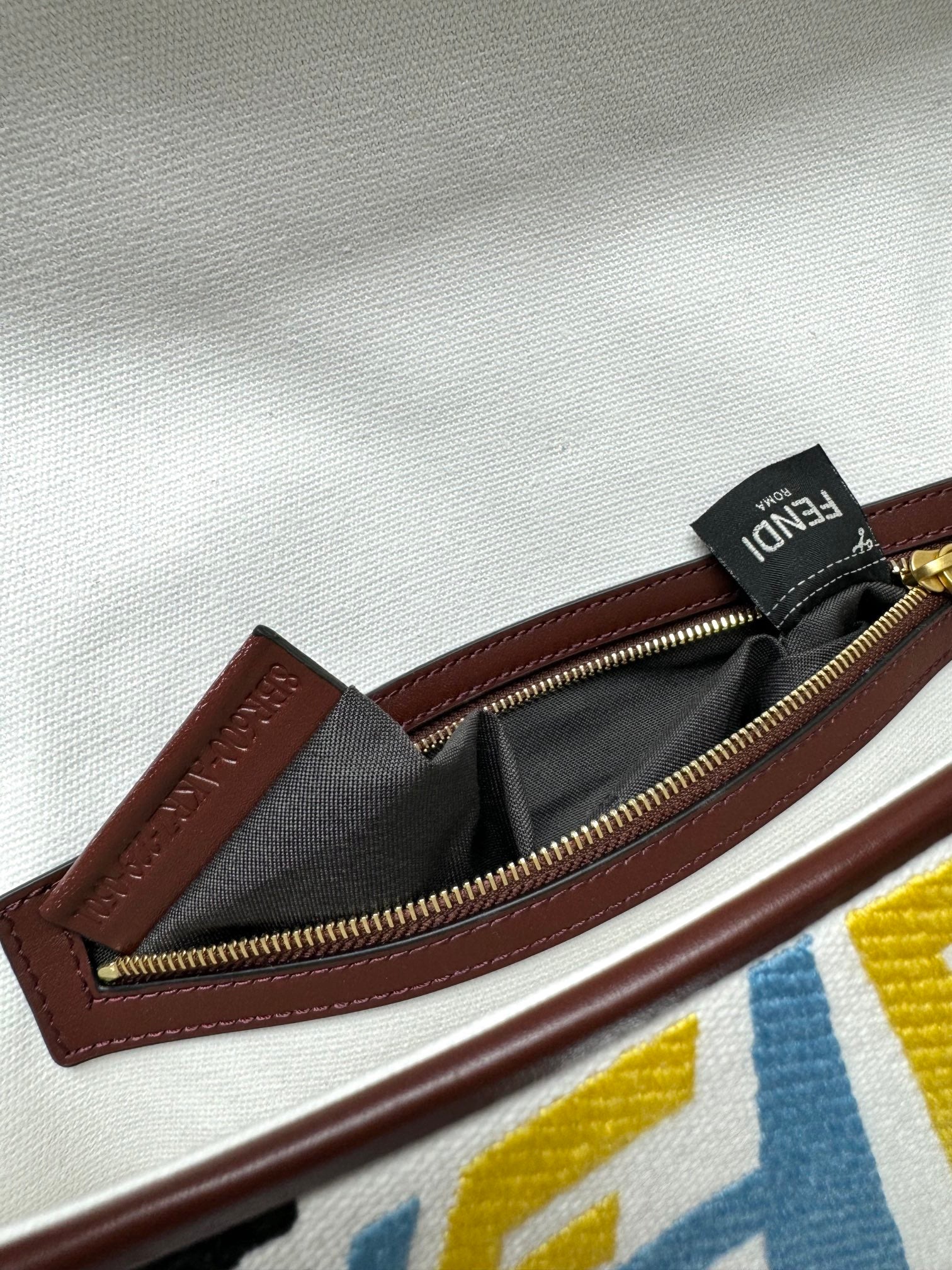 Close-up of zipper pull and maroon leather trim inside a crossbody bag