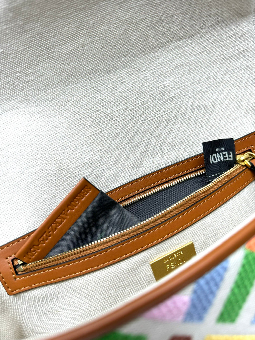 Beige canvas zip pocket with brown leather trim, gold zipper pull and dark logo tag