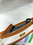Beige canvas zip pocket with brown leather trim, gold zipper pull and dark logo tag