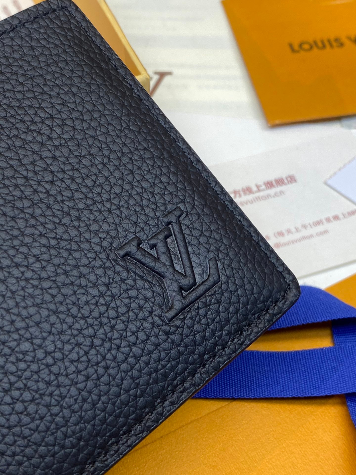 Small leather wallet corner with embossed LV-style logo, textured finish