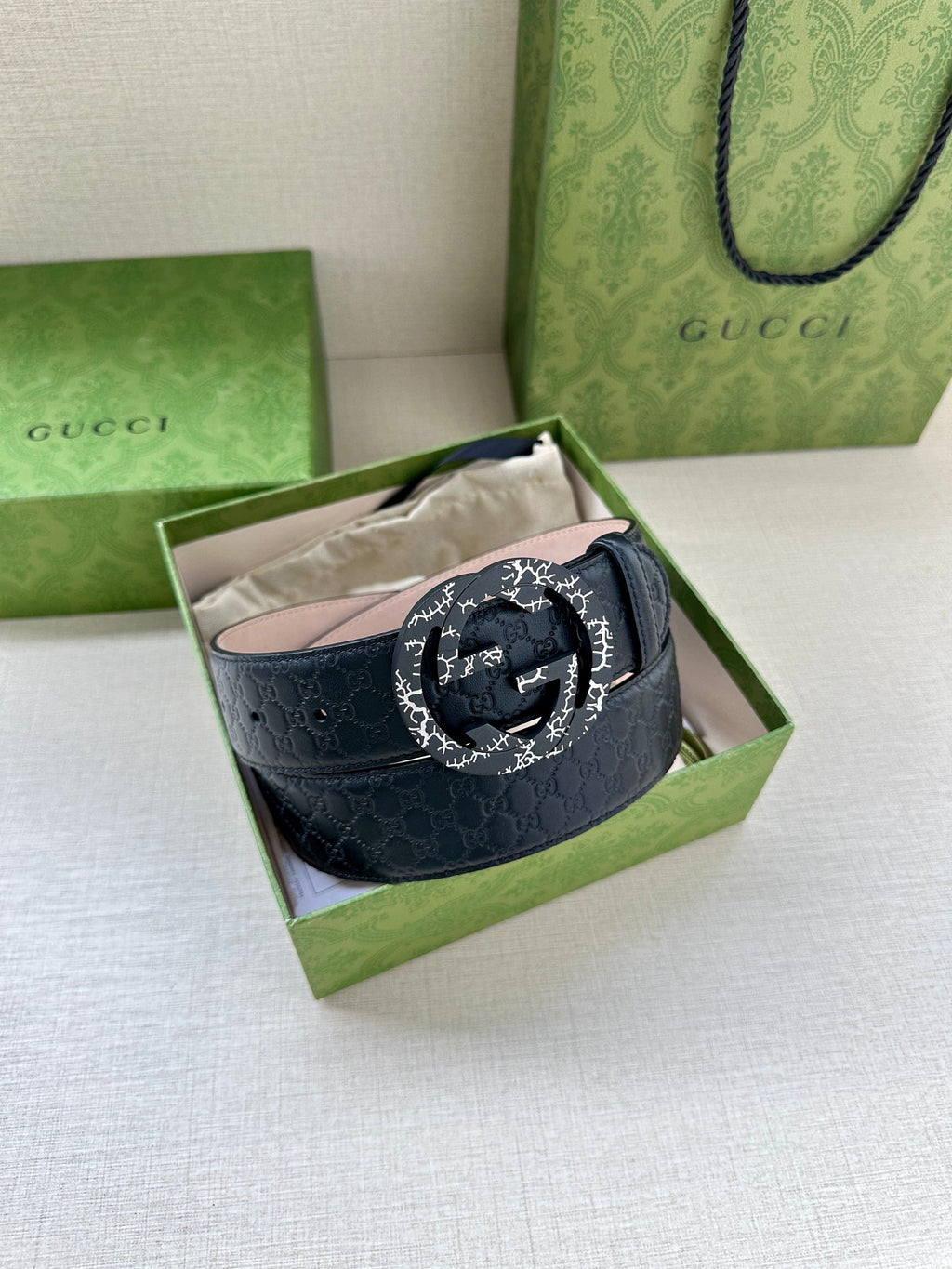 Dark blue leather belt with silver logo buckle inside a green-lined box