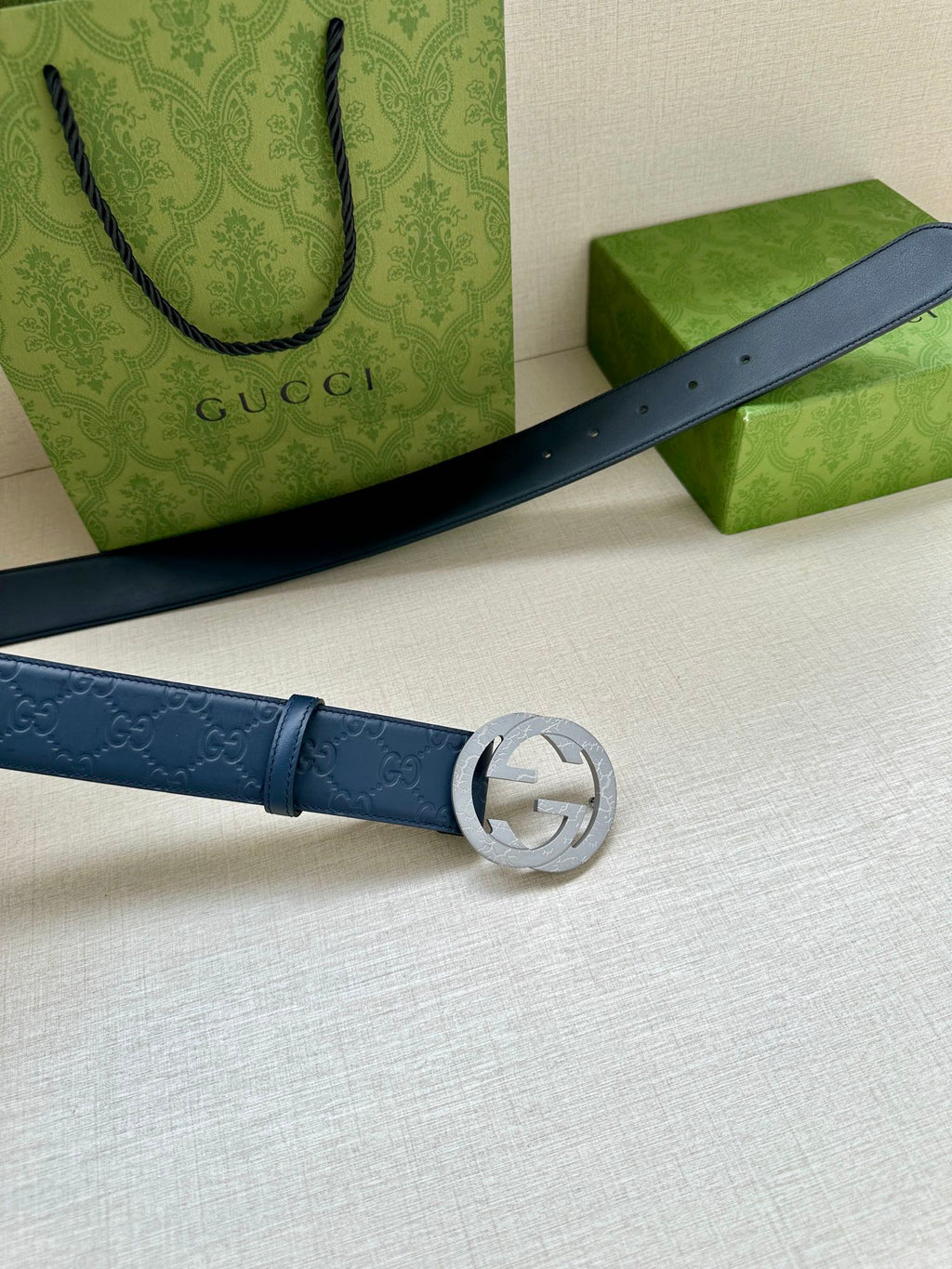 Gucci belt laid flat in dark blue leather with embossed logo and circular GG buckle