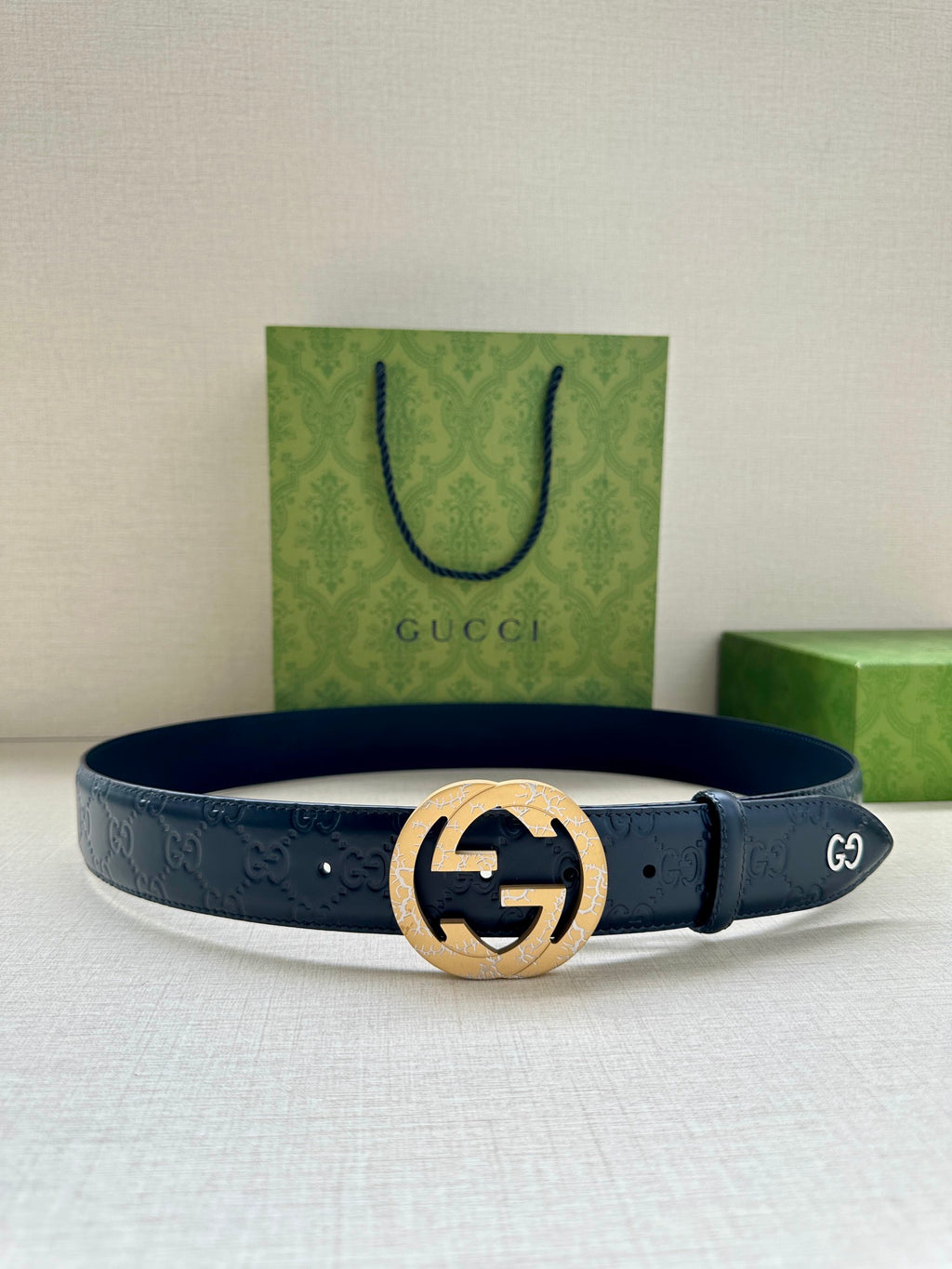 Gucci belt with dark blue leather and embossed pattern, featuring a gold-toned round buckle
