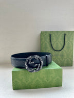 Gucci belt resting on a box, dark blue embossed leather with a dark round logo buckle