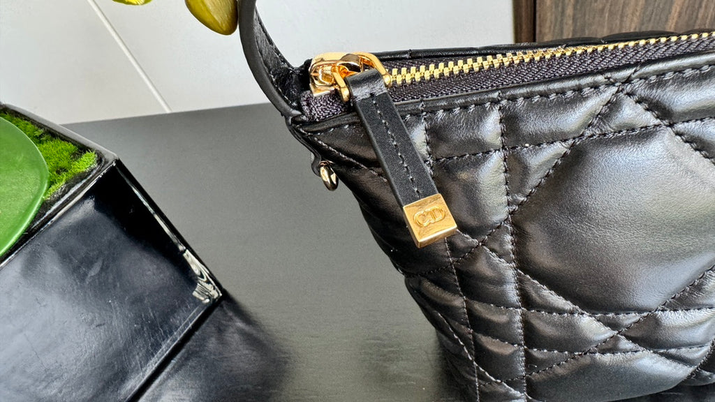 Black quilted handbag close-up of gold zipper pull and stitched trim