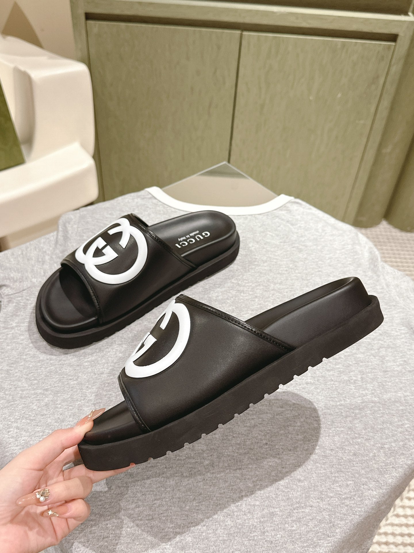 Black slide sandals with white GG logo straps, angled pair view