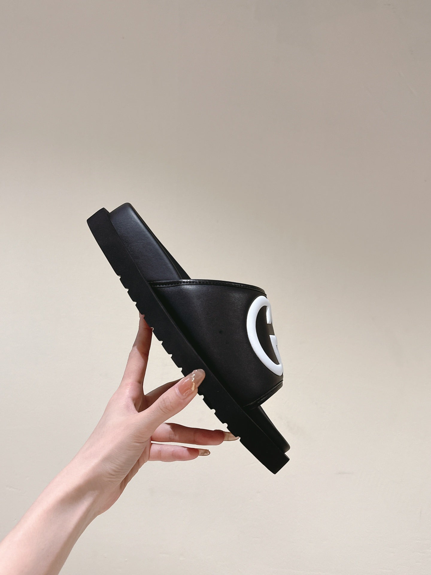 Black slide sandal with white GG logo on strap, lifted side view of one shoe