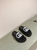 Black slide sandals with white GG logo, shown side-by-side on a light floor