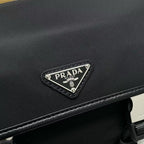 Prada black bag flap with silver triangular logo plaque and textured fabric trim.