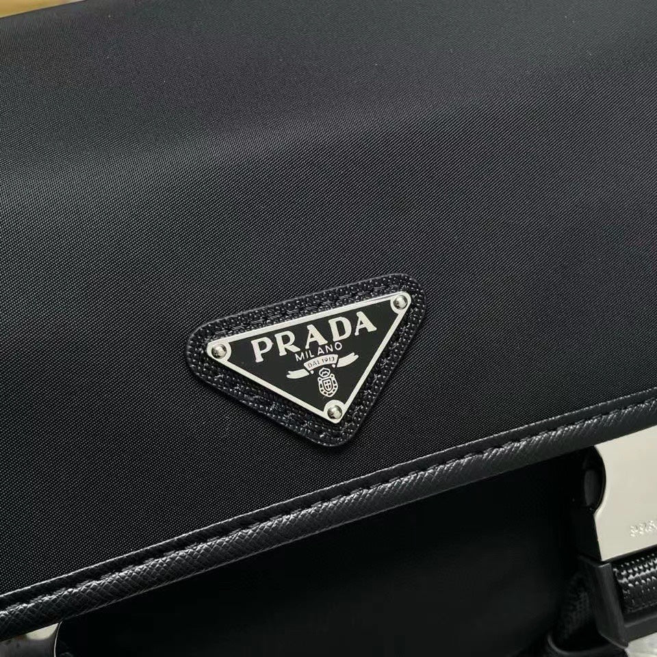Prada black bag flap with silver triangular logo plaque and textured fabric trim.