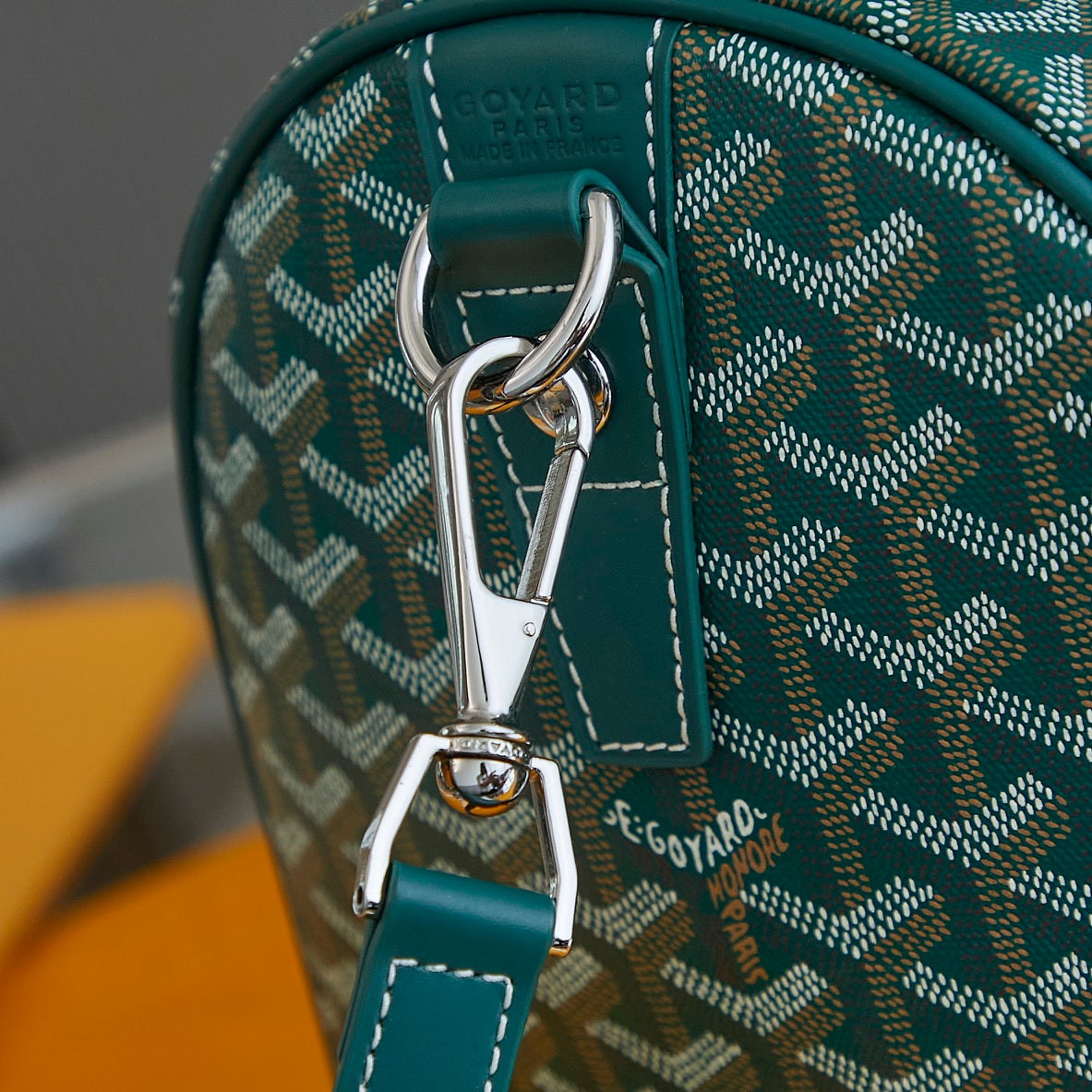 Goyard bag close-up: teal leather handle with silver clasp on patterned canvas
