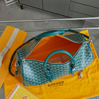 Goyard bag in teal with white pattern, open top showing orange interior lining