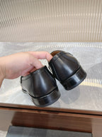 Prada unisex black loafers held side-by-side, back view of heels