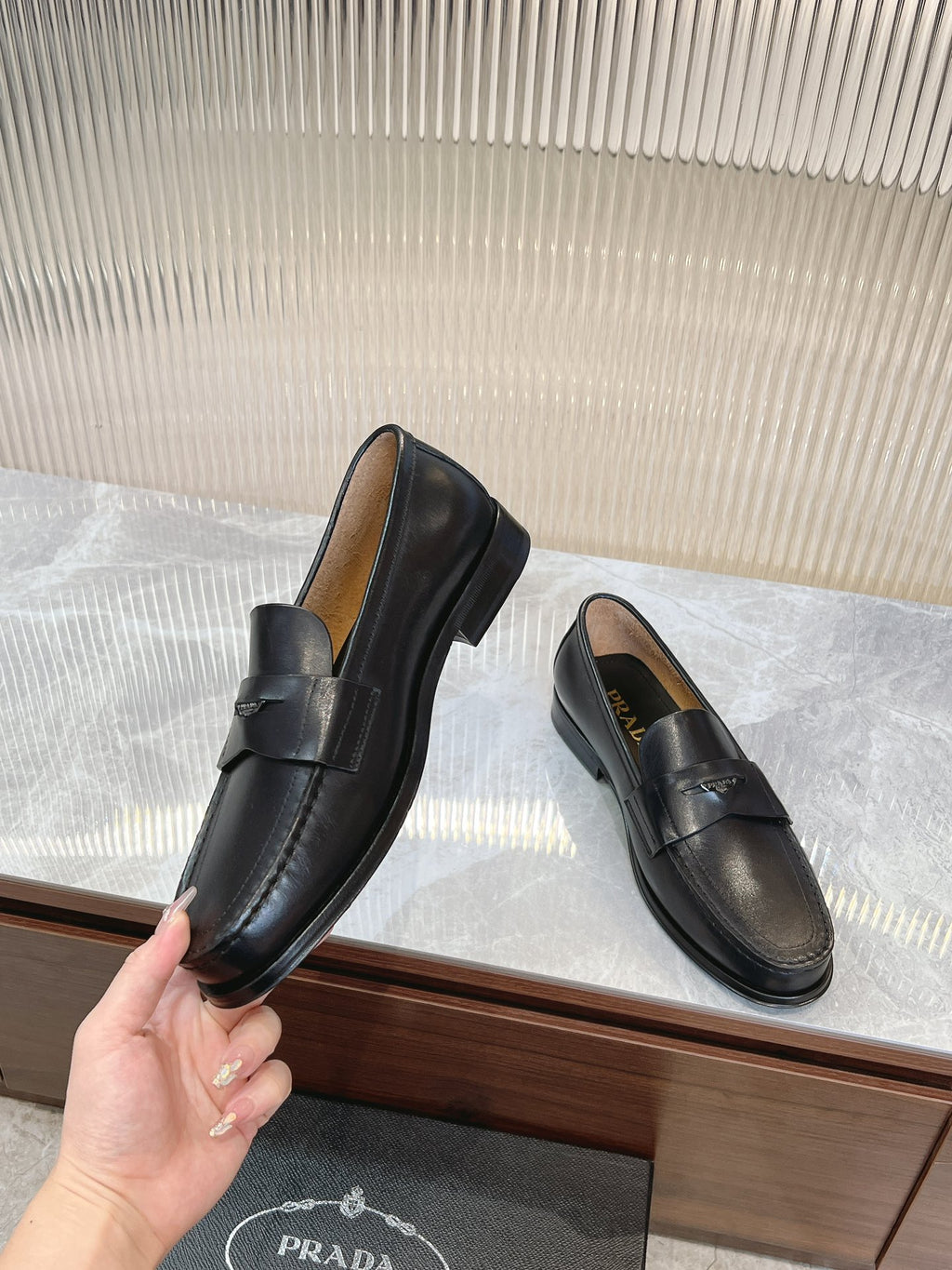 Prada unisex black loafers held in hand, rounded toe and strap detail