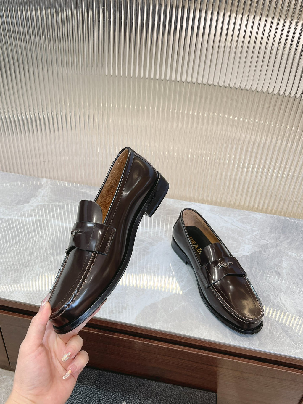 Prada unisex leather loafers, dark brown, held up by the heel and toe