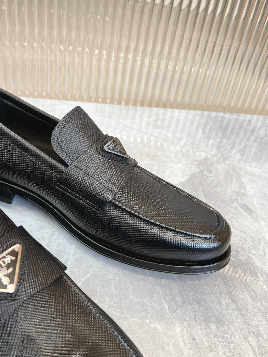 Prada unisex loafer close-up, dark textured upper, metal emblem on strap