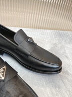 Prada unisex loafer close-up, dark textured upper, metal emblem on strap