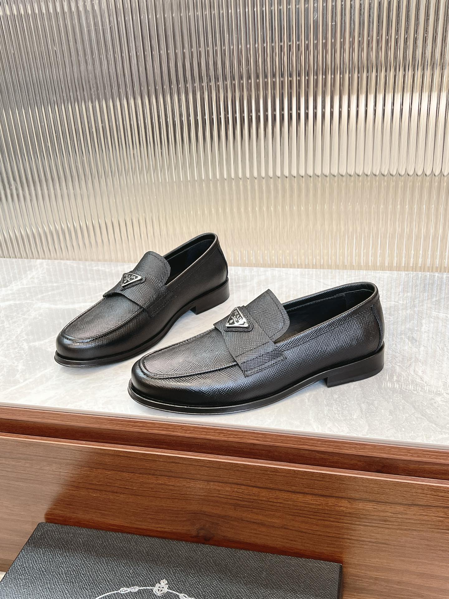 Prada unisex loafer pair, dark textured leather, low block heel, metal logo detail