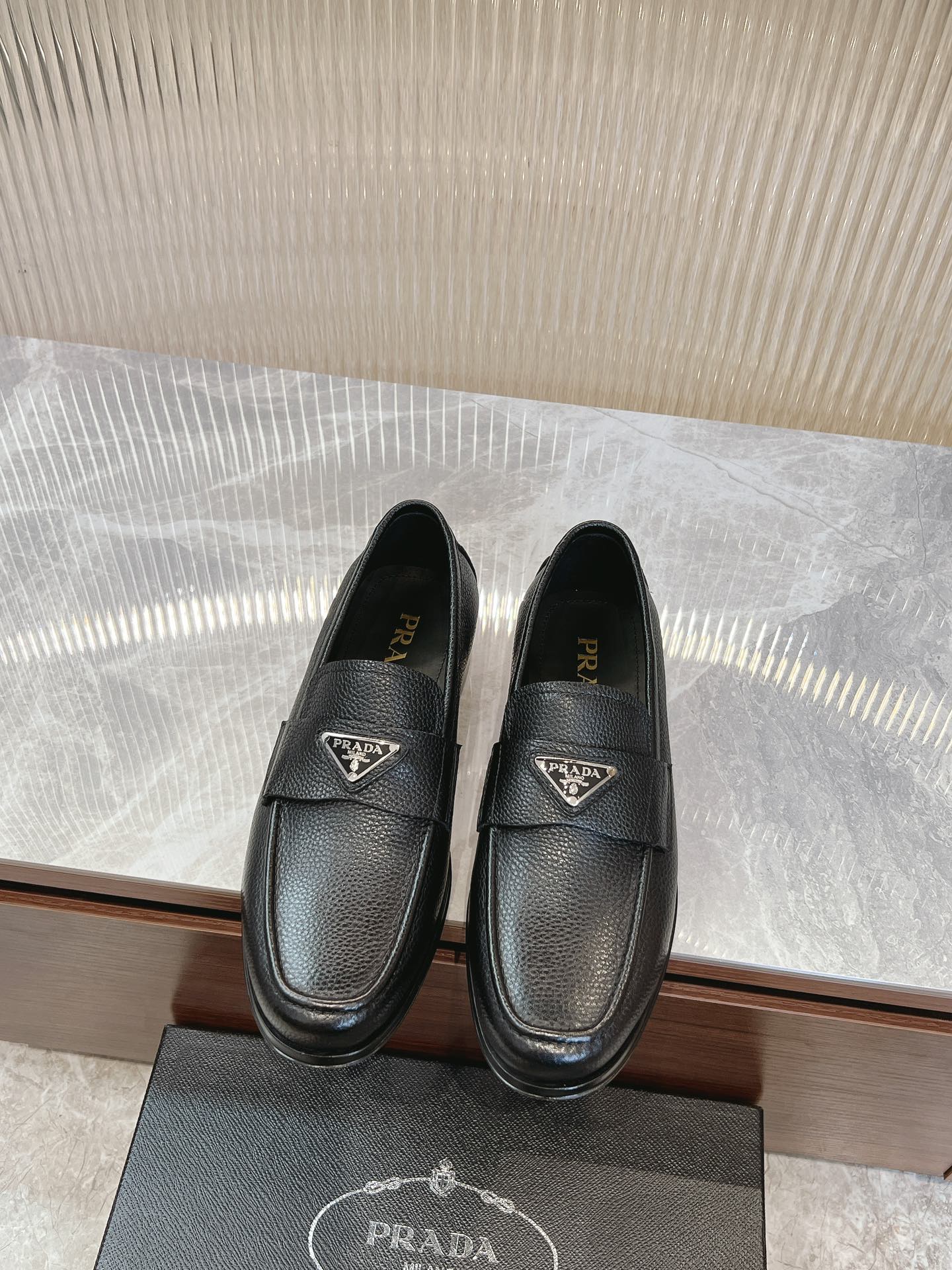 Prada unisex loafers in dark leather, metal logo badge on the vamp, slip-on style