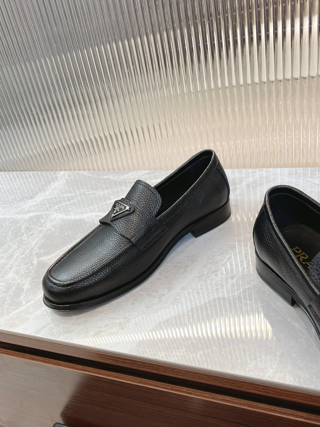 Prada unisex loafers in dark leather, low heel sole and metal logo badge on strap