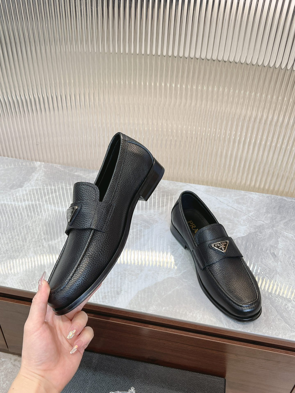 Prada unisex loafers in dark leather, front strap with metal logo badge, side angles