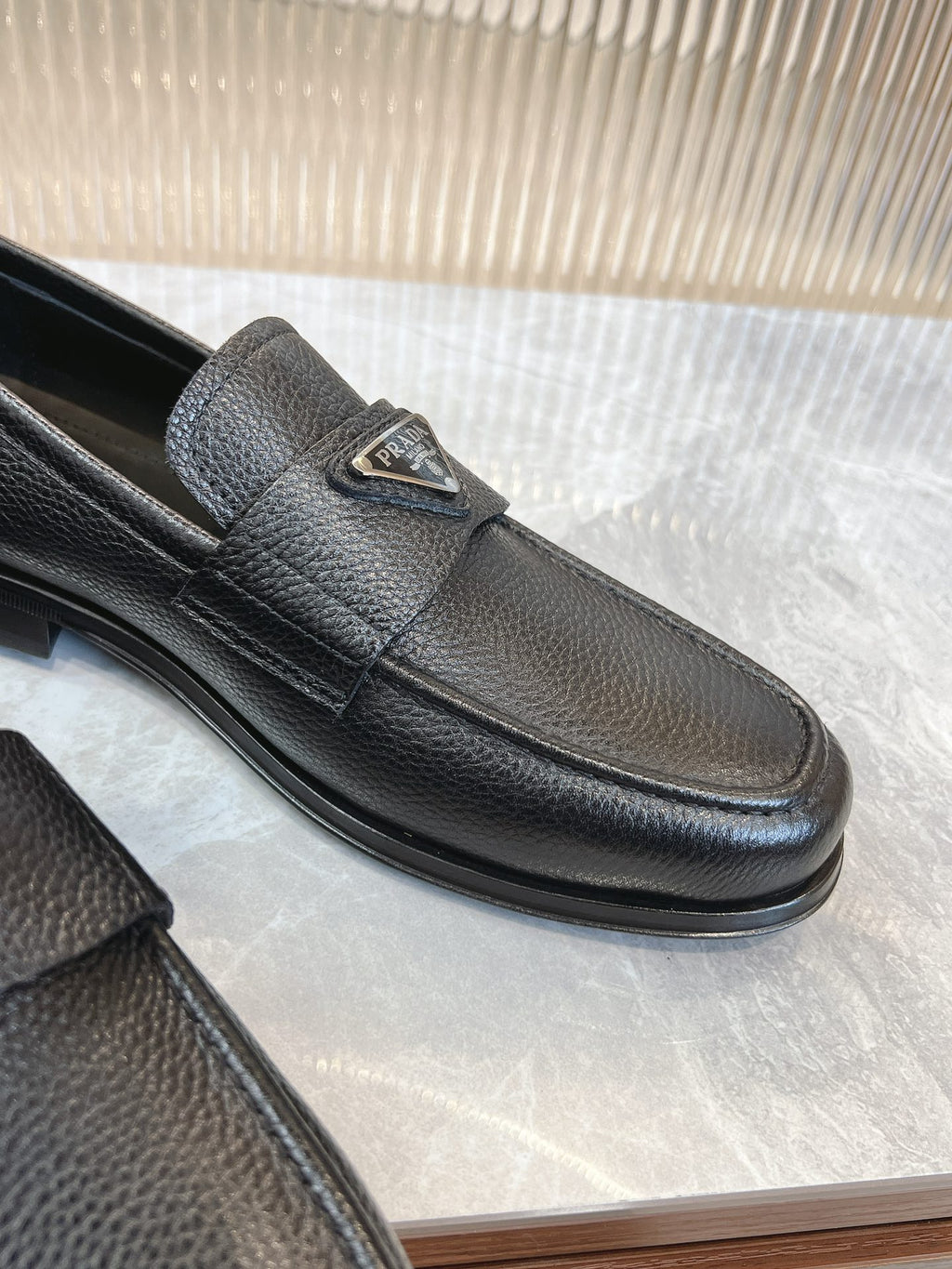 Prada unisex loafers in dark leather, close-up of metal logo badge on front strap