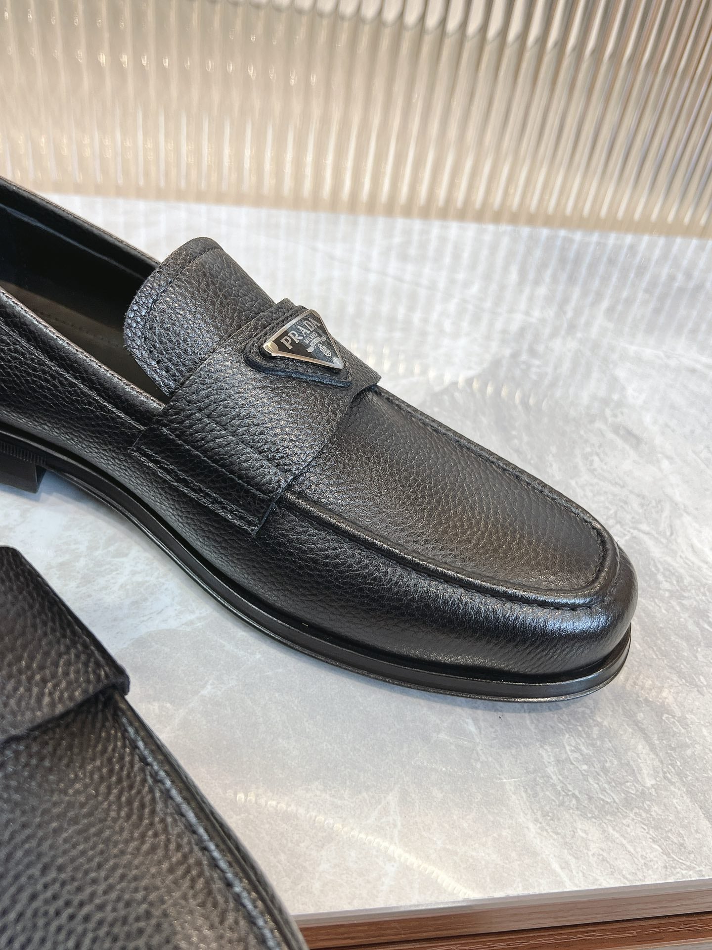 Prada unisex loafers in dark leather, close-up of metal logo badge on front strap