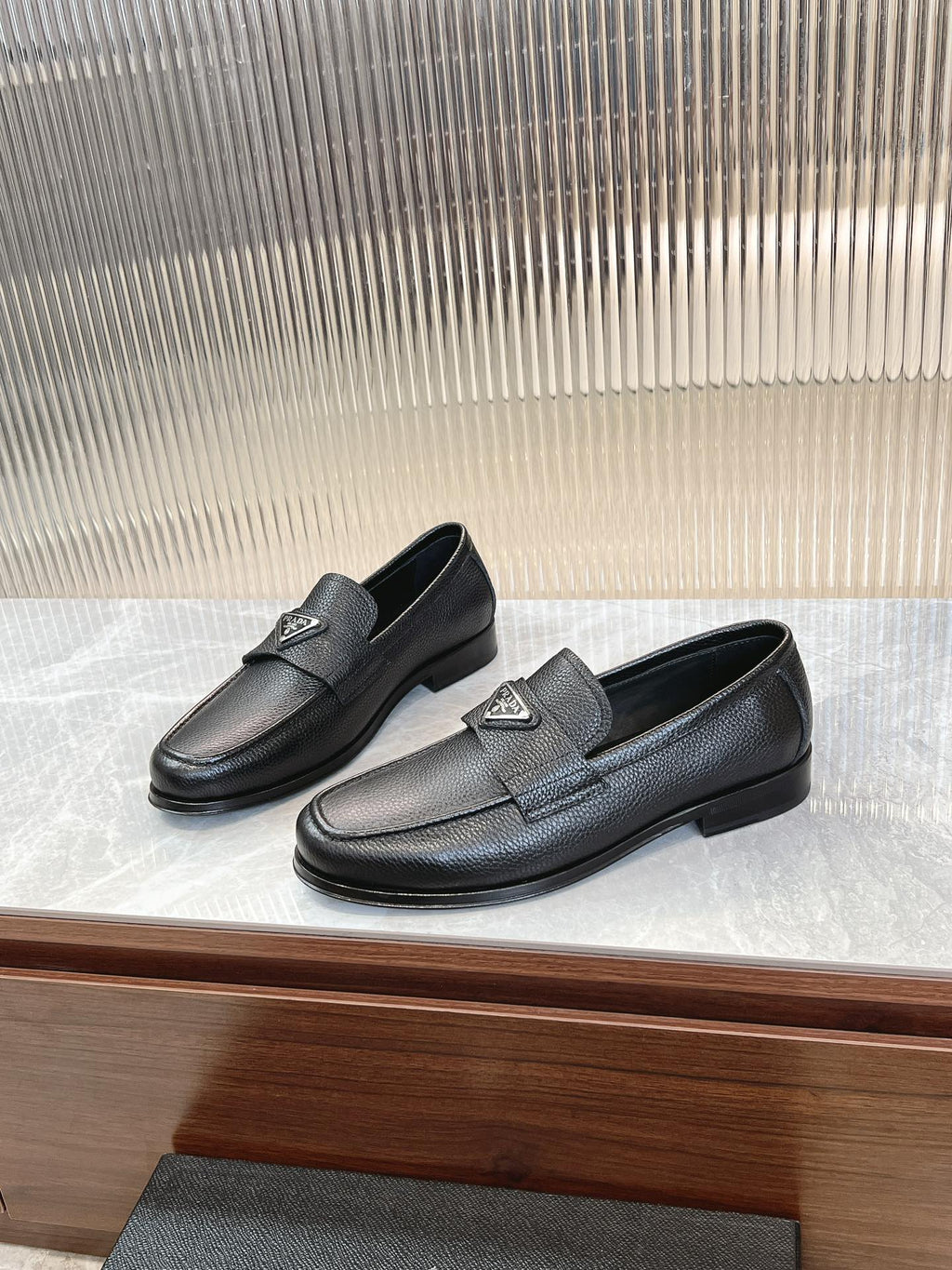 Prada unisex loafers in dark textured leather, metal logo badge on the strap