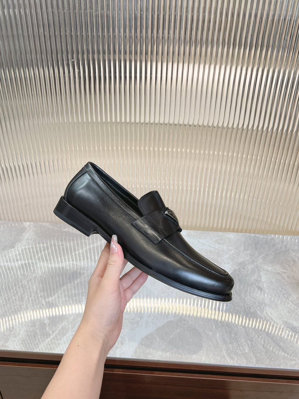 Black leather loafer with strap and square logo badge, side view.