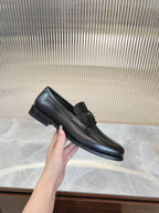 Black leather loafer with strap and square logo badge, side view.