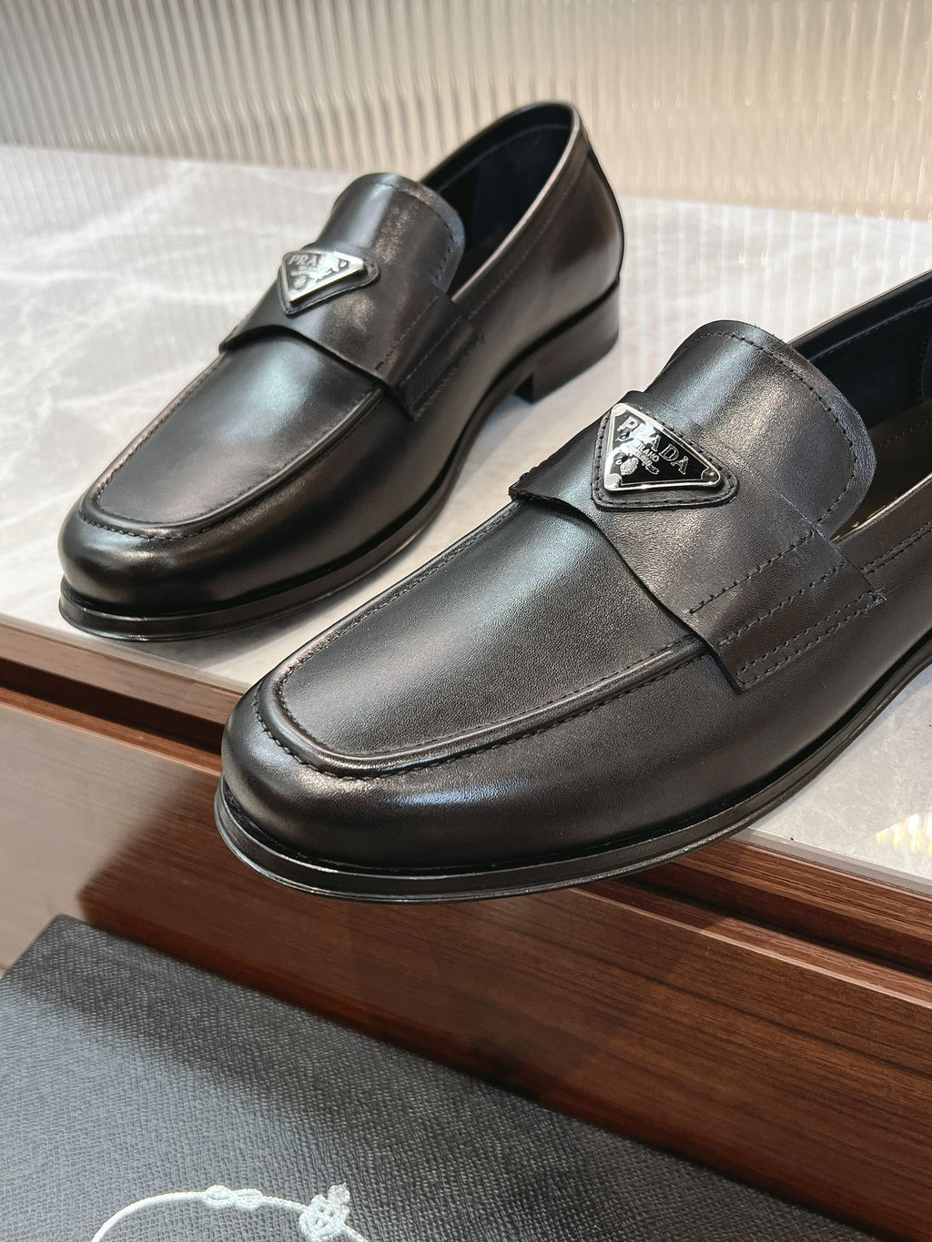 Black leather loafer pair with metal logo plate and strap seam detail.