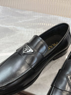 Black leather loafer with metal logo badge and Prada gold-toned insole text.