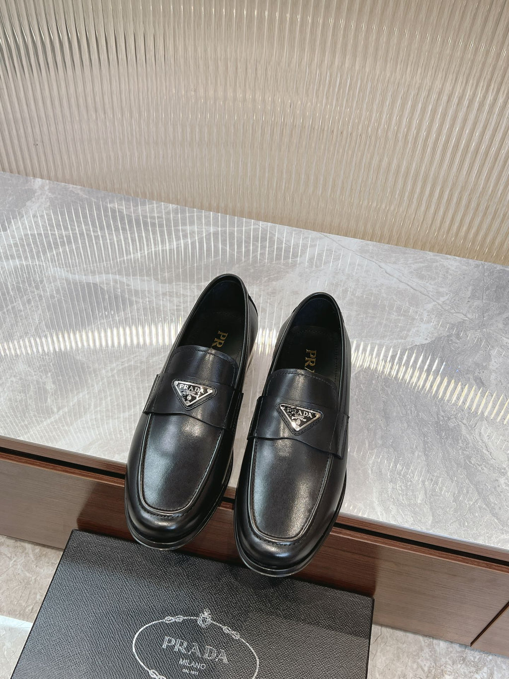 Black leather loafer with metal logo emblem, penny-style strap and low sole.