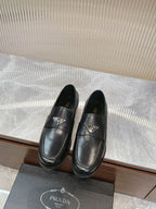 Black leather loafer with metal logo emblem, penny-style strap and low sole.