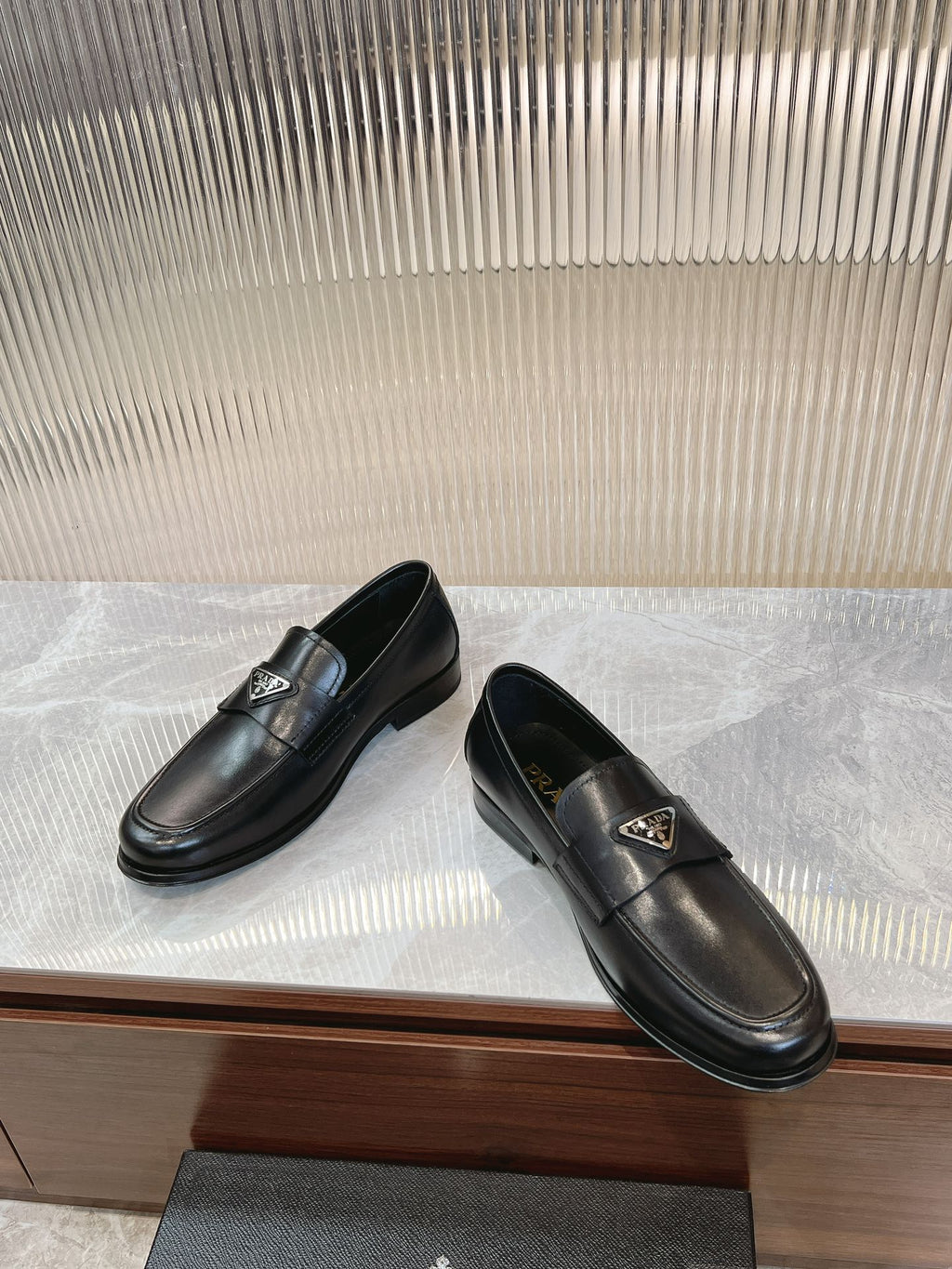 Black leather loafer pair on display, metal logo plate on strap.