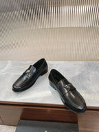 Black leather loafer pair on display, metal logo plate on strap.