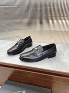 Black leather loafers with silver-toned logo badge and stitched strap detail.