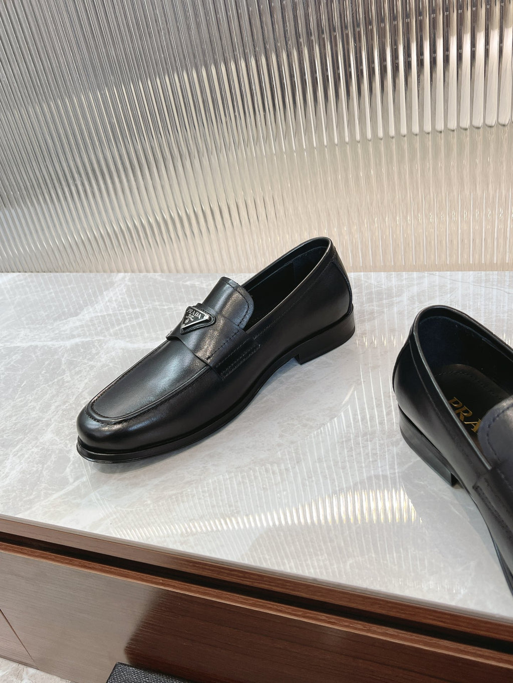 Black leather loafer pair, rounded toe and low heel with logo detail.