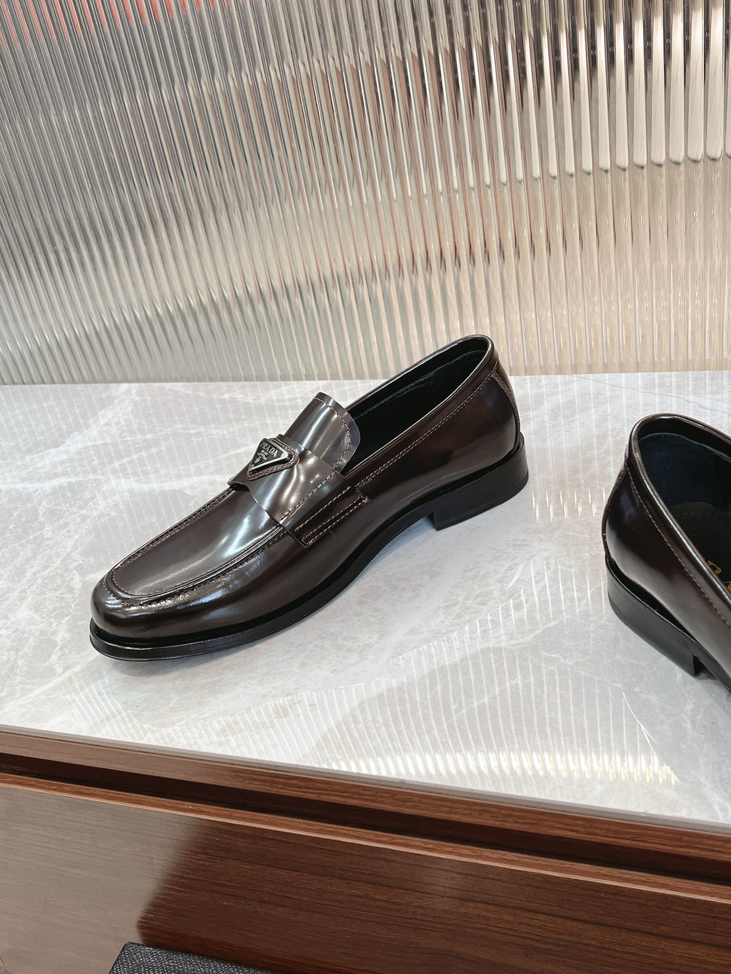 Dark brown leather Prada unisex loafer with metal emblem on front strap