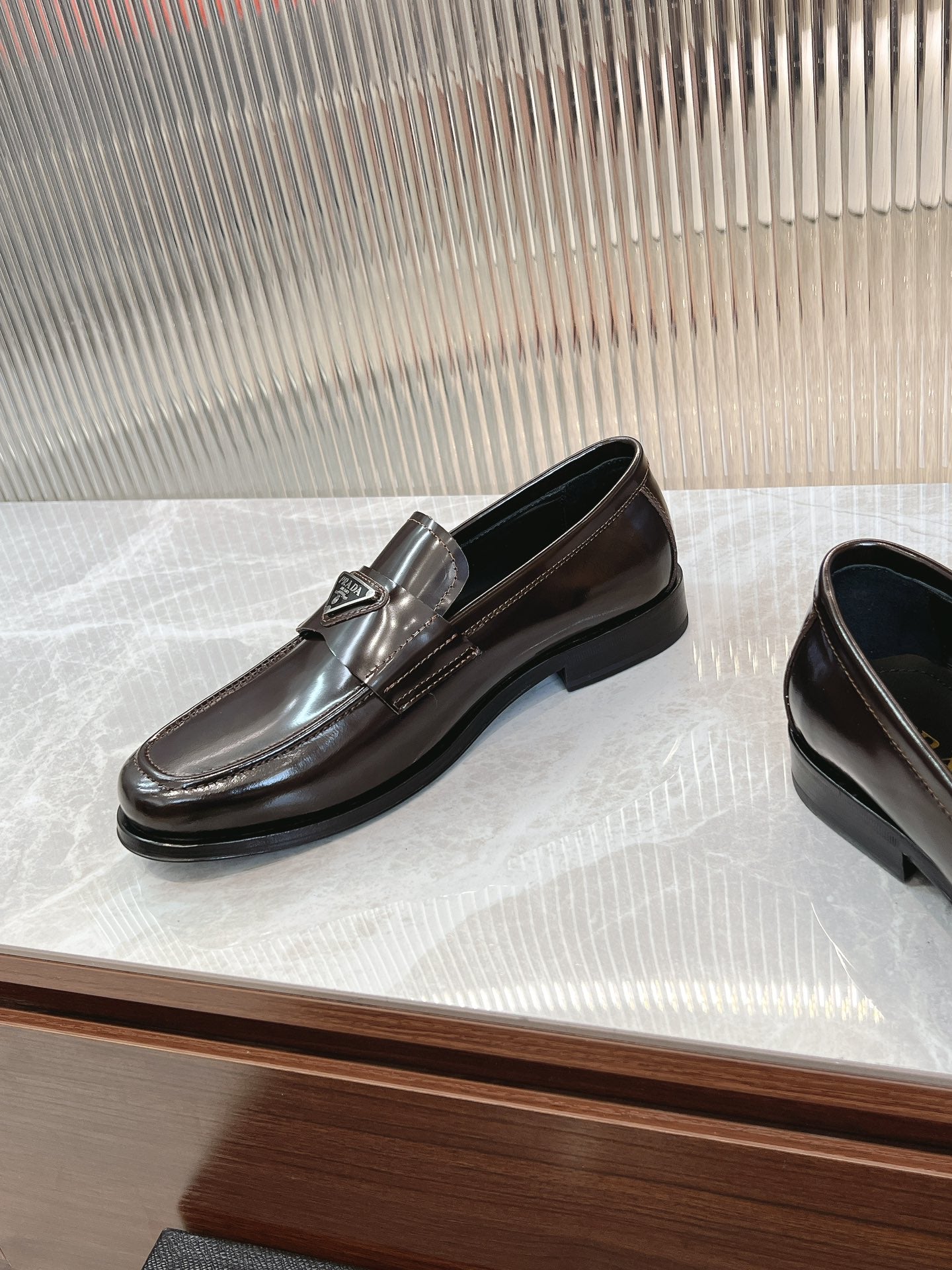 Dark brown leather Prada unisex loafer with metal emblem on front strap