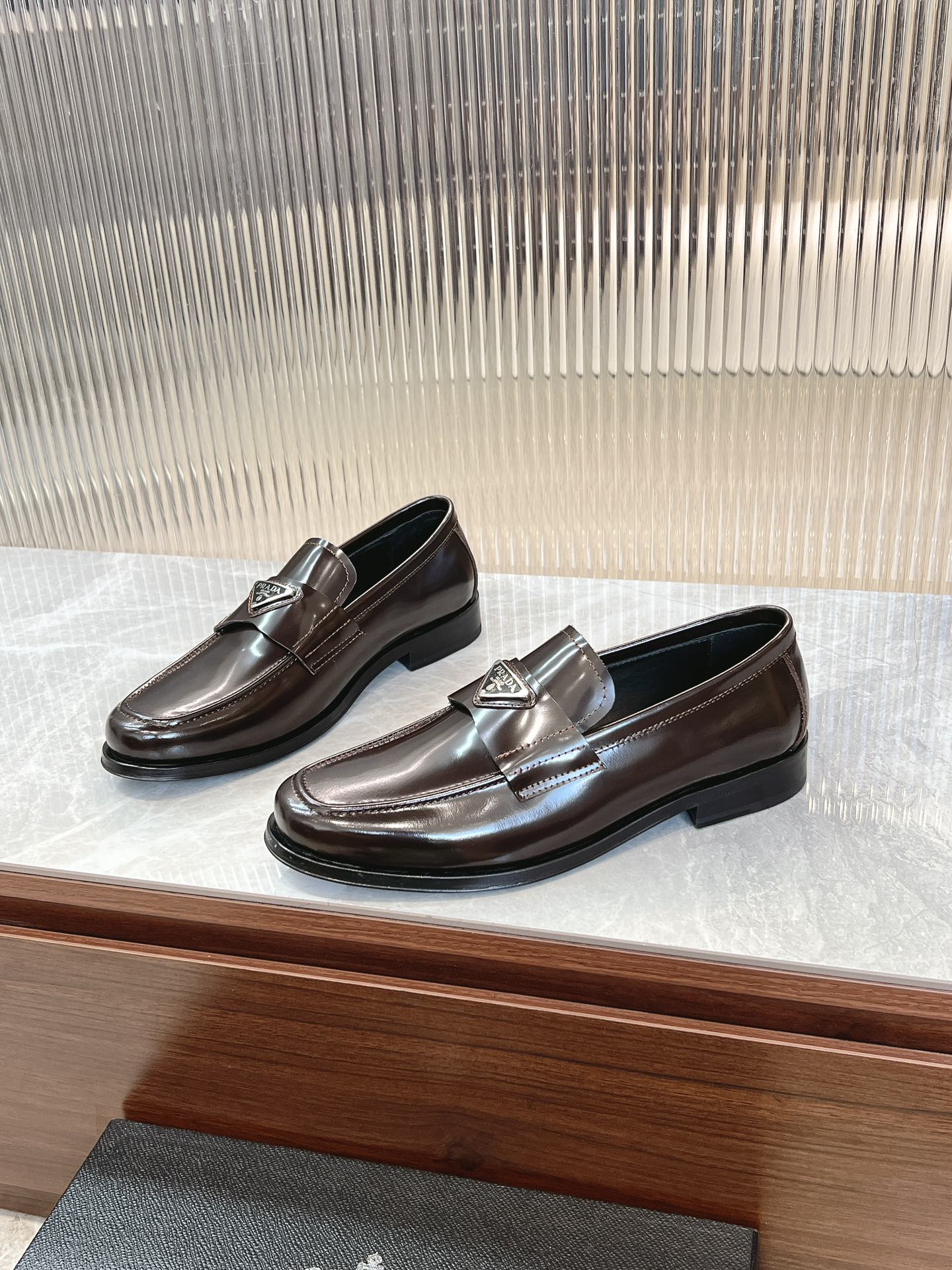 Dark brown leather Prada unisex loafers with metal emblem and glossy finish