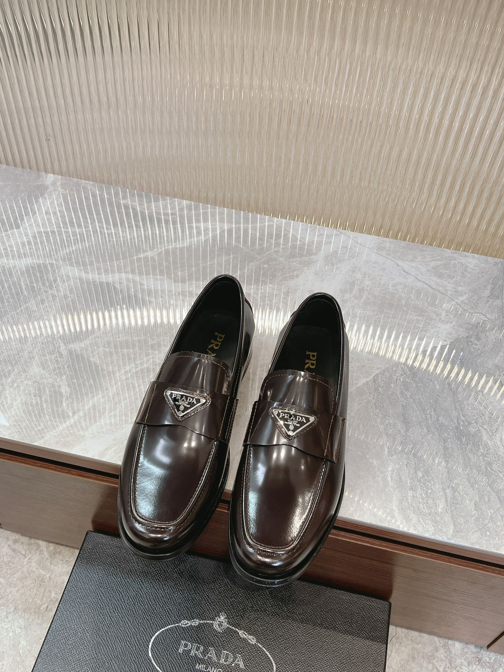 Dark brown leather Prada unisex loafers with metal emblem at front