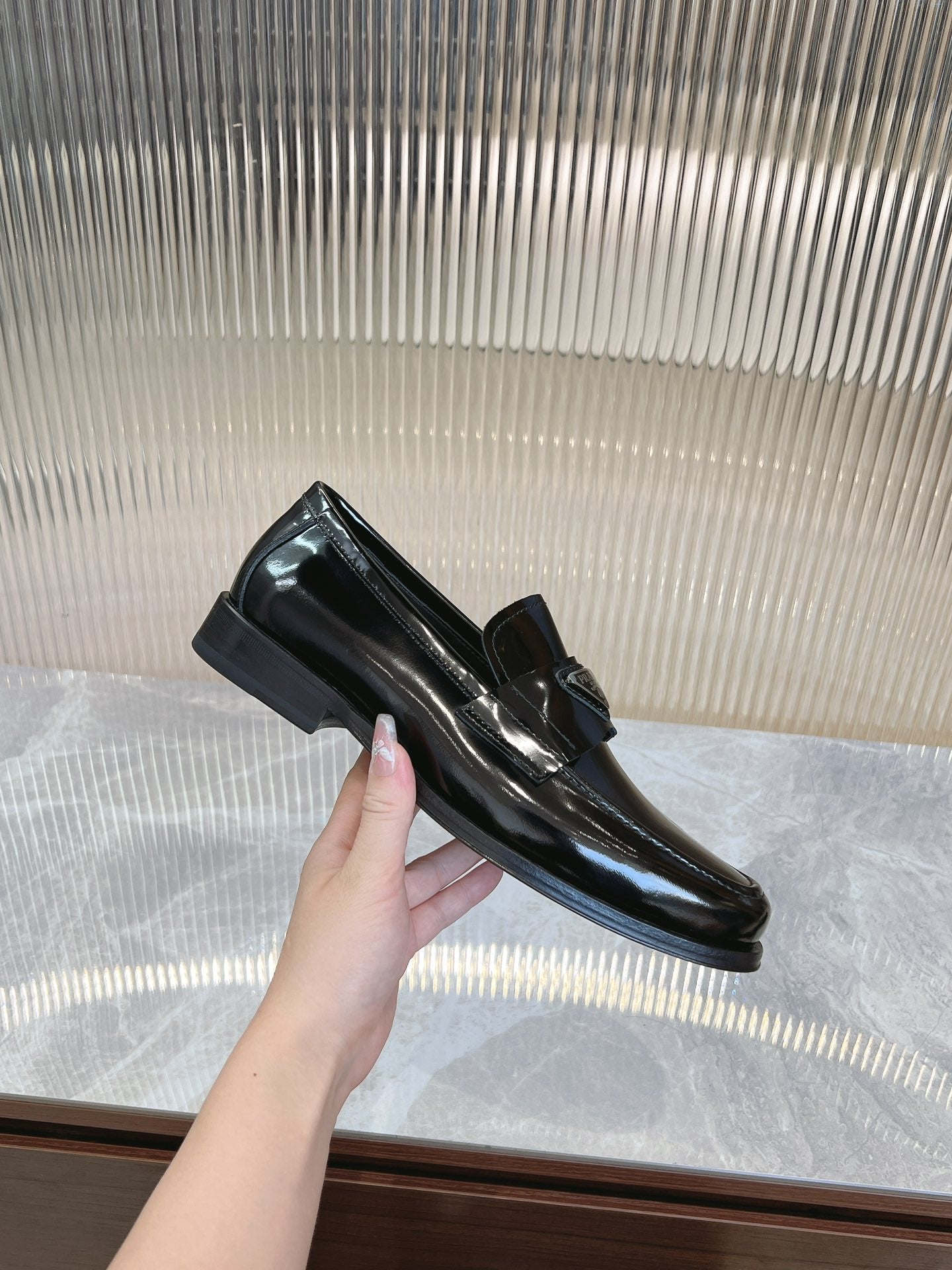 Prada unisex loafers in dark patent leather, hand lifting one shoe