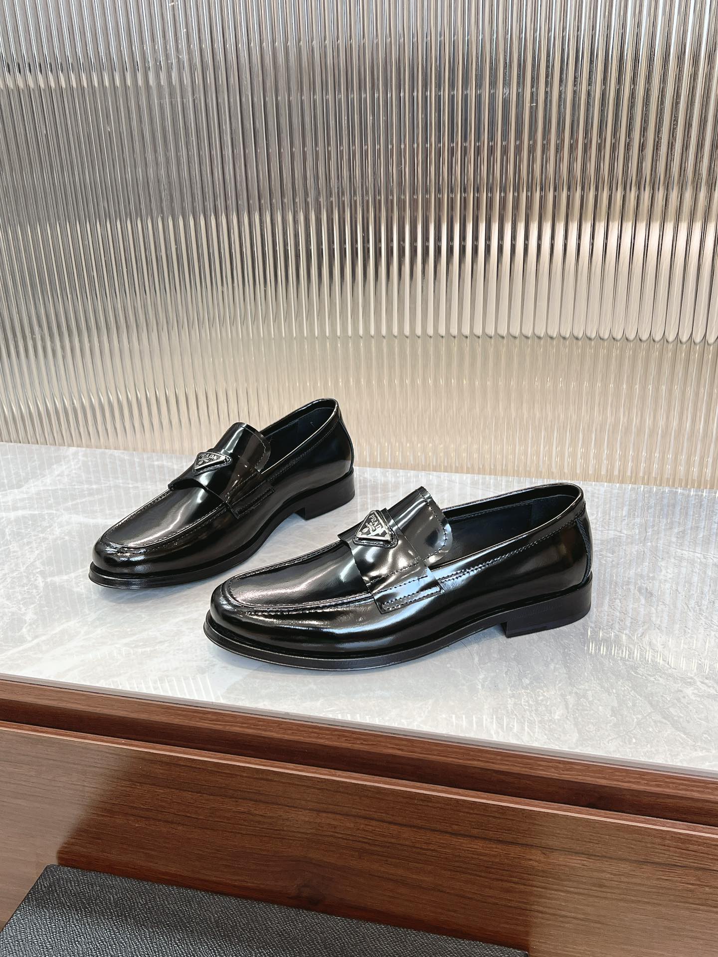 Prada unisex loafers in dark patent leather with metallic buckle, angled view