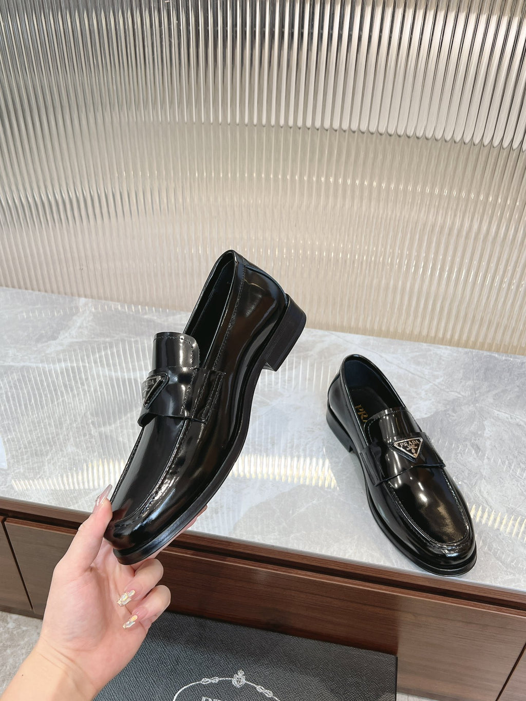 Prada unisex loafers, dark patent leather, hand holding one pair
