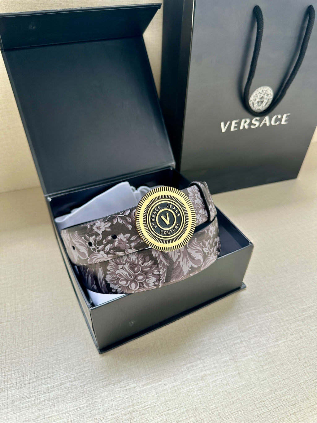Versace belt in open box: gray floral strap with gold round logo buckle