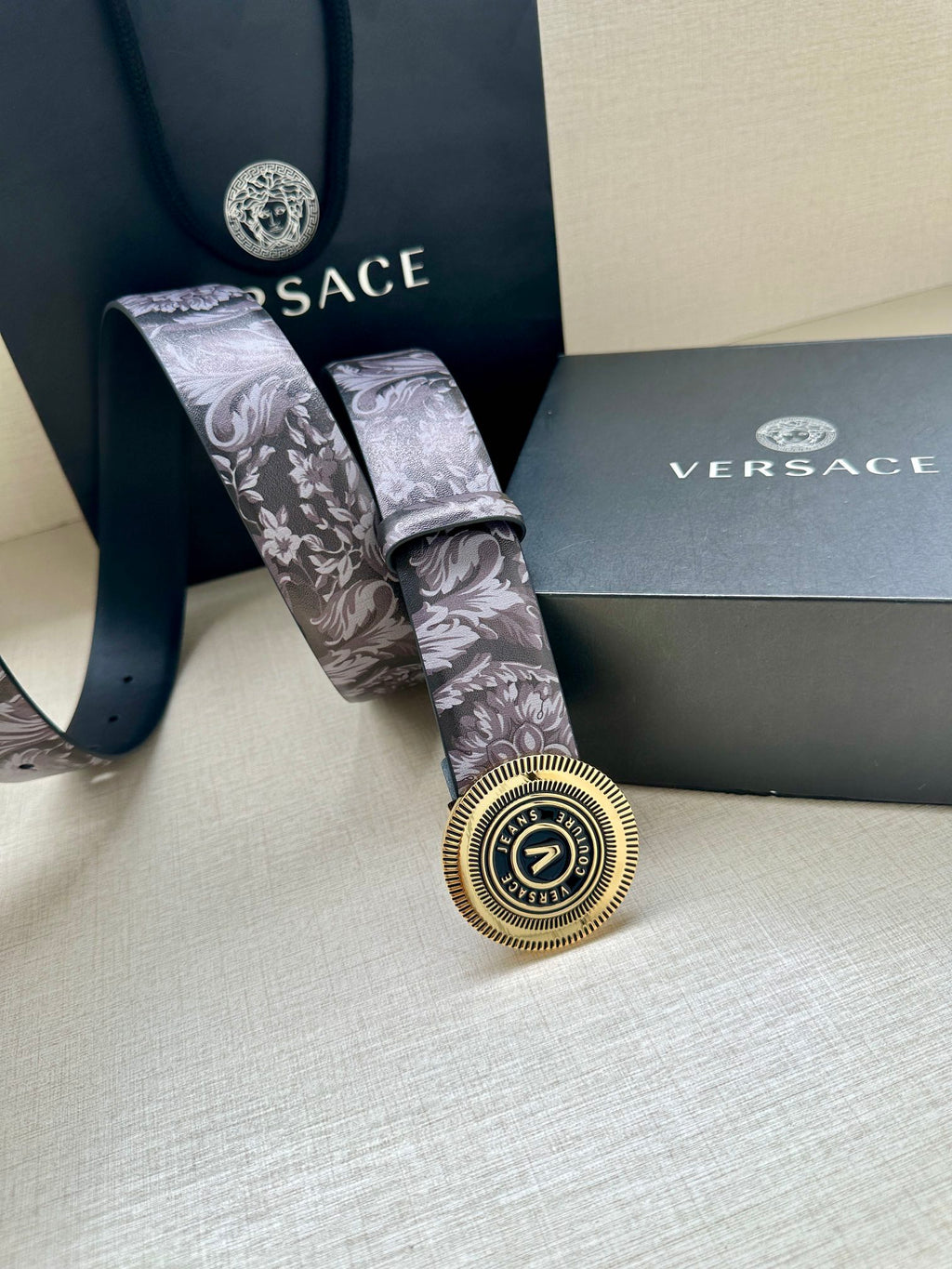 Versace belt with gray floral strap and gold round V buckle, laid flat